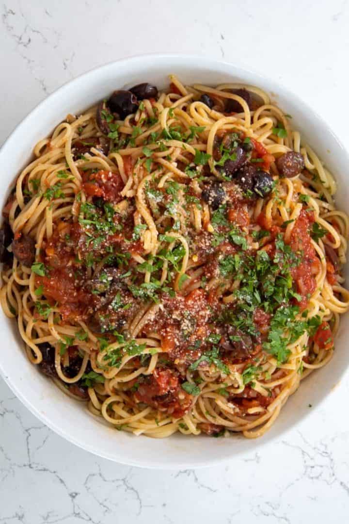 This Pasta Puttanesca Recipe is made with onion, garlic, white wine, tomatoes, capers, olives, and topped on al dente spaghetti.