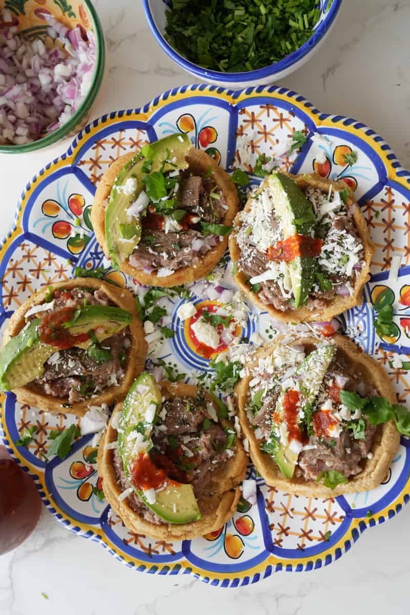 This Mexican Sopes Recipe is made with carne asada, refried beans, maseca, avocado and cotija cheese and cooked to perfection.