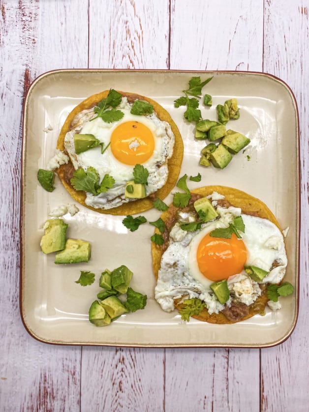 These Authentic Huevos Rancheros are fried tortillas topped with a Sunny-side egg with salsa verde, cilantro, avocado, cheese and sour cream.