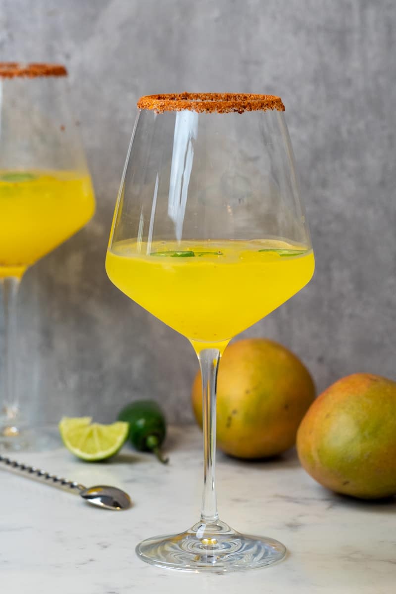 This Mango Jalapeño Margarita on the rocks is made with mango juice, jalapeno pepper, tequila blanco, triple sec, angostura bitters, tajin, and limes.