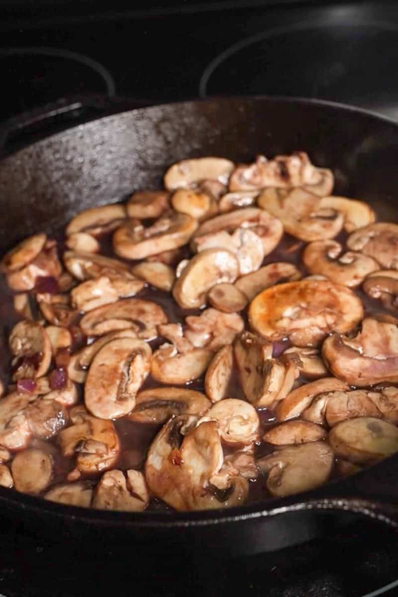 Sliced mushrooms and chopped red onion browning in a cast-iron skillet