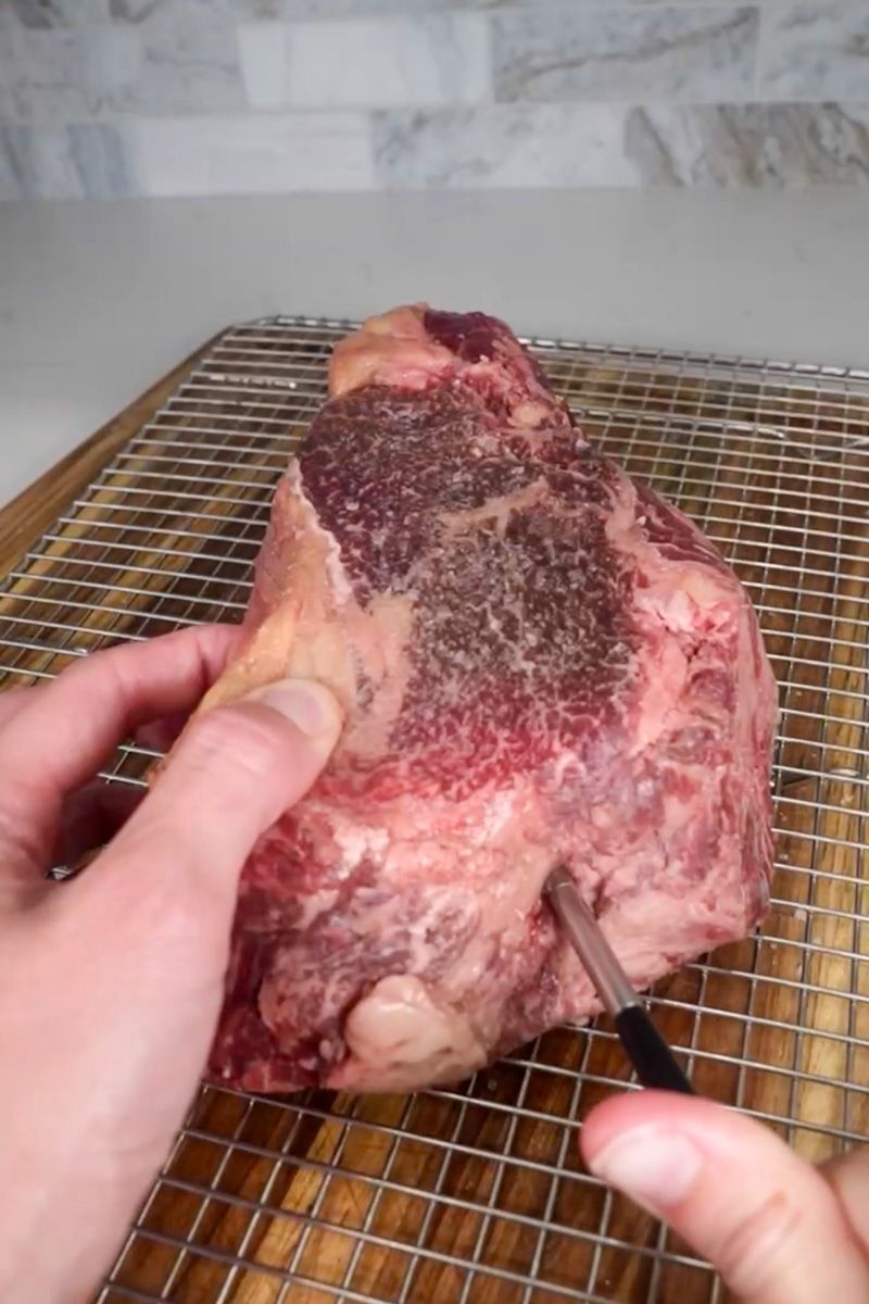 Seasoned 2-inch steak resting on a wire rack before cooking