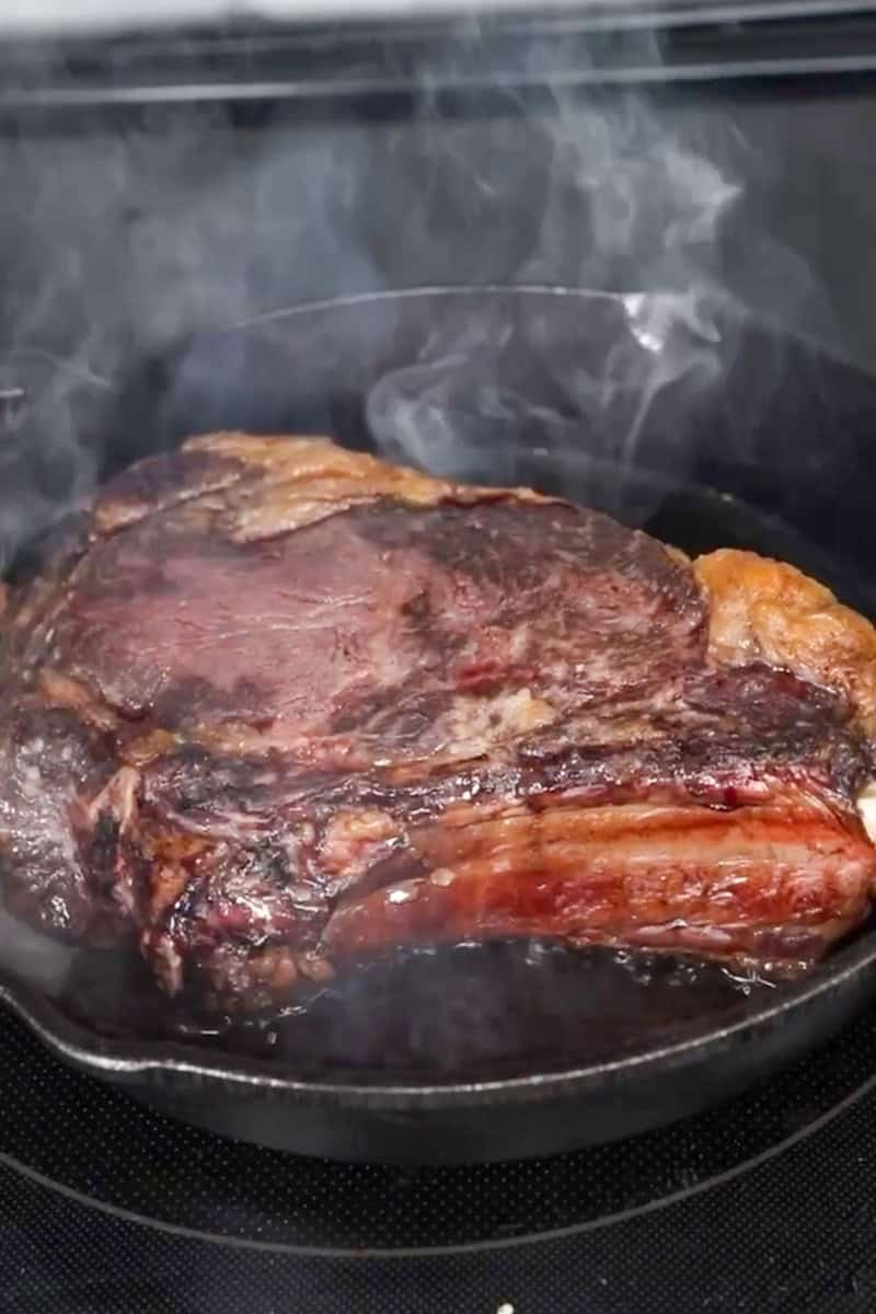 Thick steak developing a browned crust in a cast-iron skillet