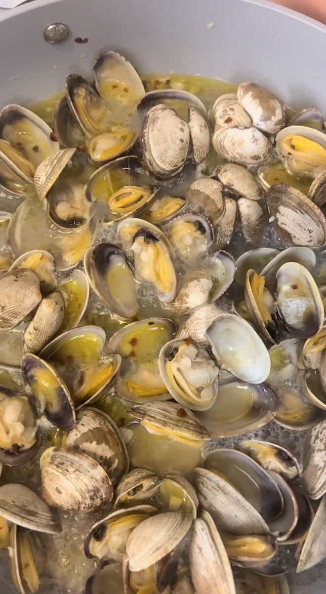 Pour in the white wine and increase the heat to high until it starts boiling. Add the clams. 
