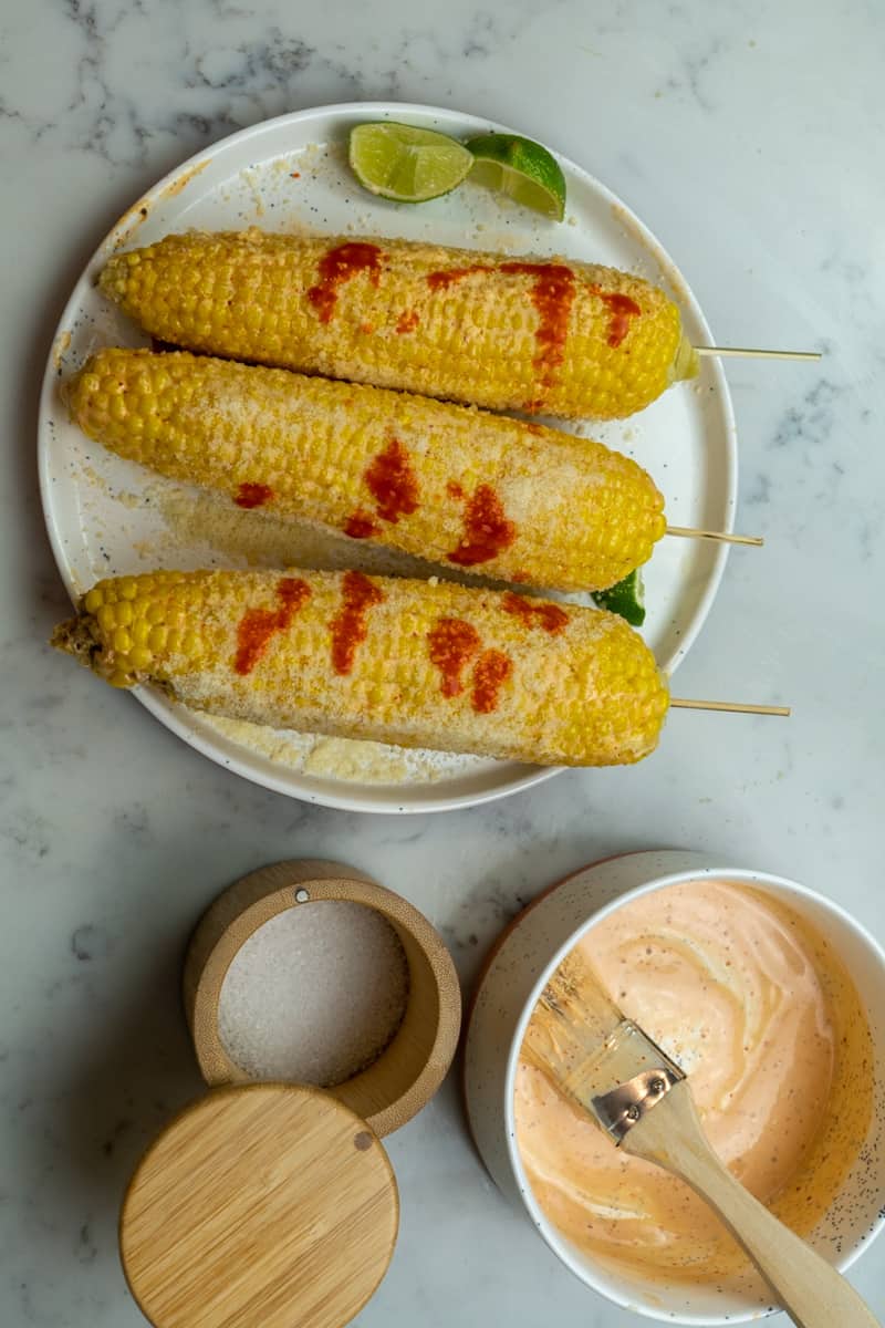 This Elote Mexicano is made with dehusked corn, mayonnaise, chili powder, hot sauce, lime juice, and topped with cotija cheese.