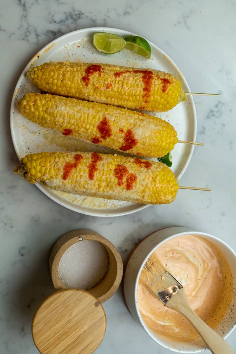 Esta Elote Mexicano Receta se prepara con elote, mayonesa, chile en polvo, salsa picante, jugo de limón y queso cotija.