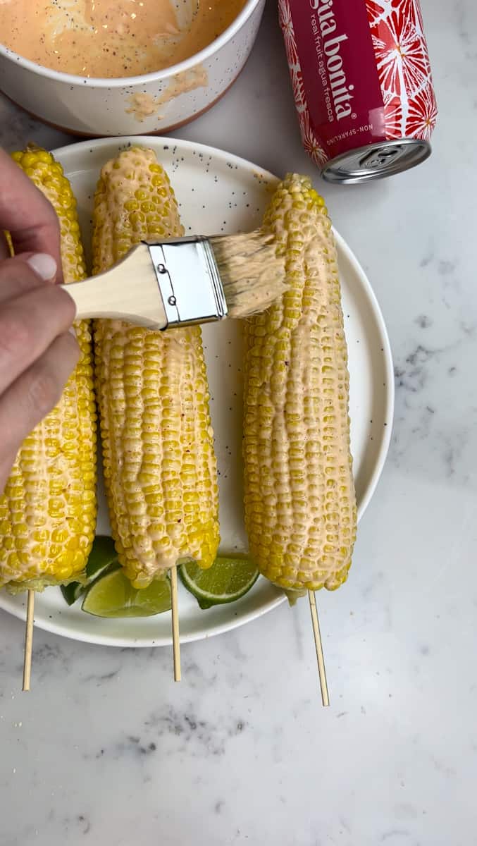 Retire el maíz del agua. Cepille la salsa sobre cada mazorca de maíz. 
