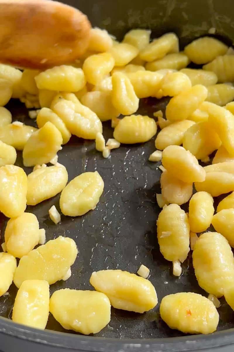 In a large pan on medium high heat, add oil and wait for it to shimmer. Toss in the garlic and toss until fragrant, about 1 minutes. Toss in the gnocchi and coat it in the oil. 