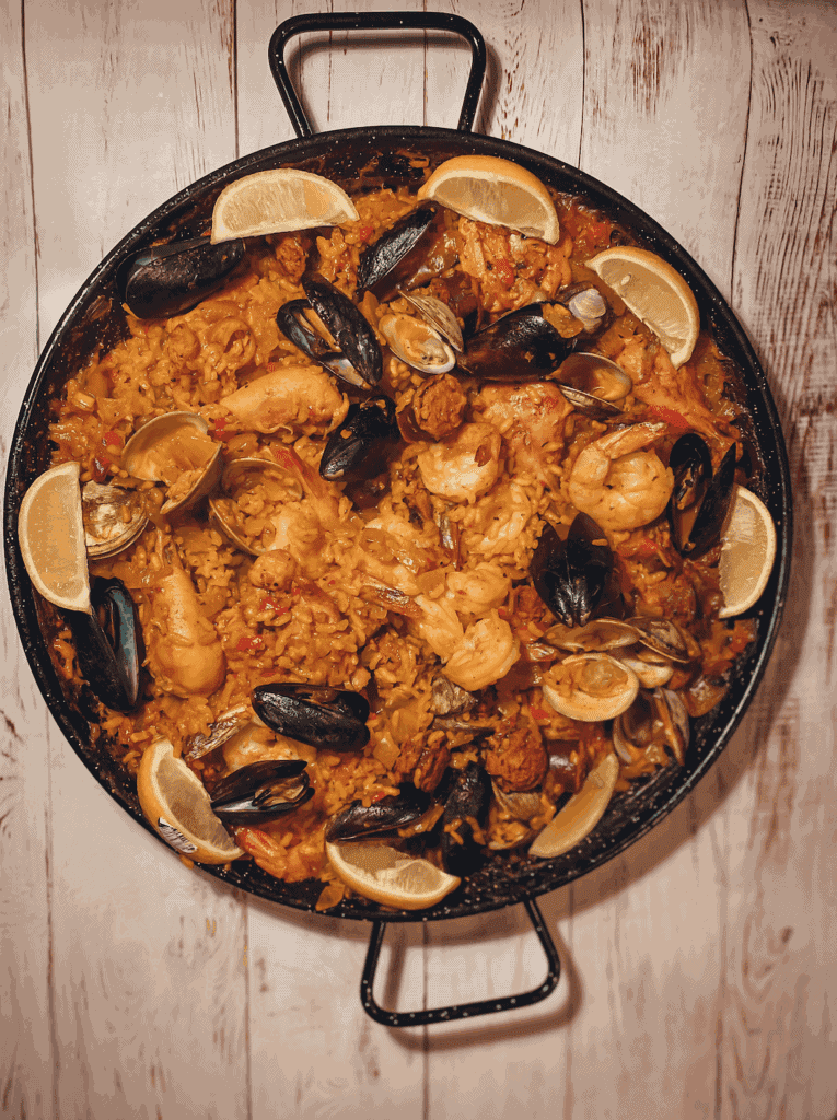 Chicken and Shellfish Paella dish contains saffron, chicken legs, bomba rice, onion, tomato sauce, chorizo, shrimp, mussels, and clams. 