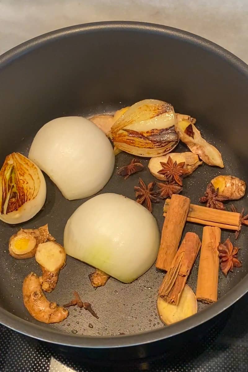 In a large stockpot over medium high heat, add the oil and wait for it to shimmer. Add the ginger and place the onion cut-side-down. Cook until charred, about 7-10 minutes. Remove and set on a plate.