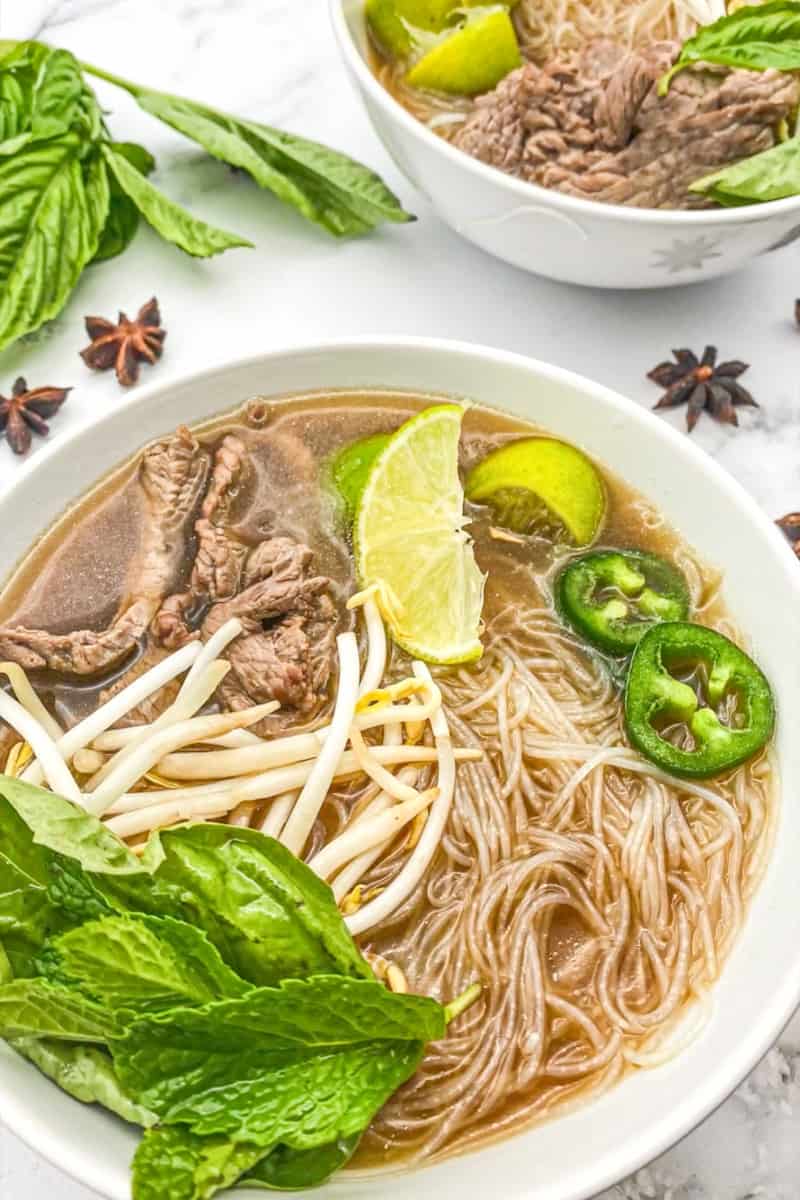 Assemble the noodles. Add the noodles in each bowl. With tongs, take the pieces of steak out of the broth and add in each bowl. Ladle the simmering hot broth into the serving bowls. Garnish with bean sprouts, limes, cilantro, jalapeños and scallions.