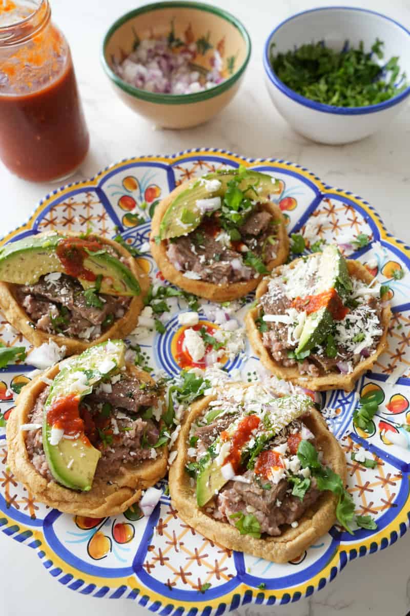 This Mexican Sopes Recipe is made with carne asada, refried beans, maseca, avocado and cotija cheese and cooked to perfection.