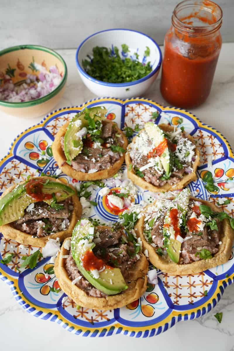 This Mexican Sopes Recipe is made with carne asada, refried beans, maseca, avocado and cotija cheese and cooked to perfection.