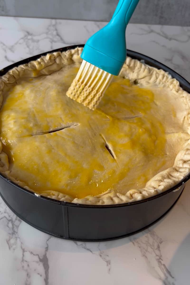 Complete the pie by cover with the puff pastry. With a fork, dock the pie and prick the pie crust with a fork. Brush egg wash over the top sheet, until coated.