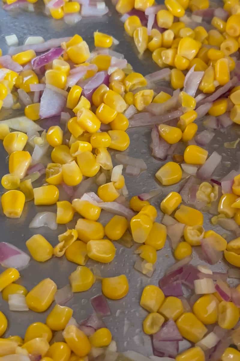 En una sartén grande caliente el aceite a fuego medio. Agregue la cebolla, el maíz y el ajo y cocine hasta que la cebolla esté suave, aproximadamente 5 minutos.