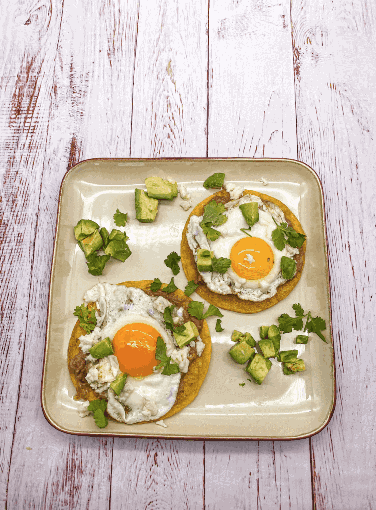 Huevos Rancheros is a fried tortilla topped with a Sunny-side egg and garnished with salsa verde, cilantro, avocado, cheese and sour cream.