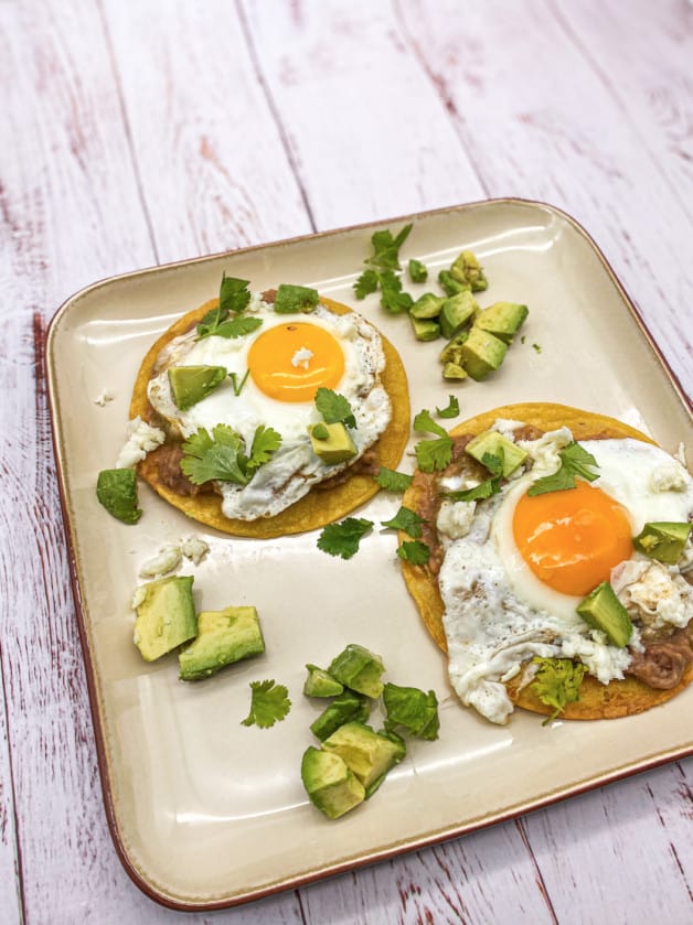 Huevos Rancheros is a fried tortilla topped with a Sunny-side egg and garnished with salsa verde, cilantro, avocado, cheese and sour cream.