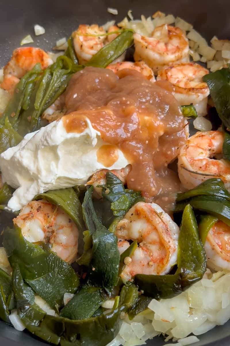 Add the shrimp in a single later and cook until the edges turn pink, about 1 minute. Flip the shrimp and cook for another minute. Remove from heat and add the sour cream and salsa verde as well as the sliced poblano peppers. 