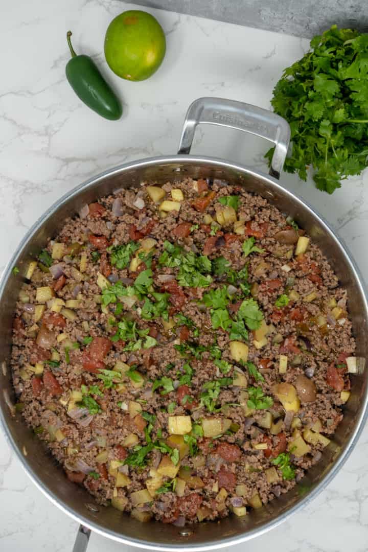 This Picadillo with Potatoes is made with ground beef, onion, jalapeños, chili powder, cumin, and garnished with cilantro and limes.