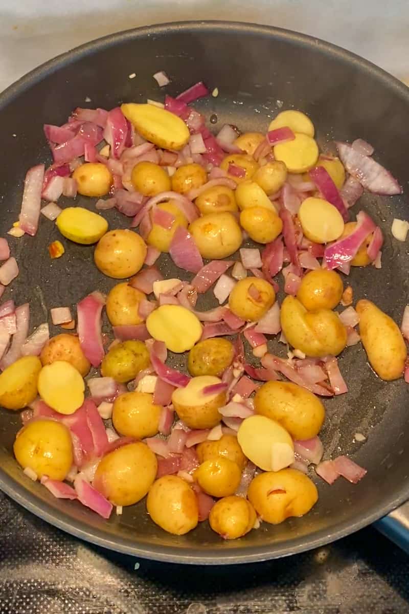 In a lidded large saucepan on medium heat, heat the olive oil and wait for it to shimmer. Add the onion and potatoes and sauté until the onions and potatoes are soft, about 10 minutes. Add garlic until fragrant, about 1 minute.