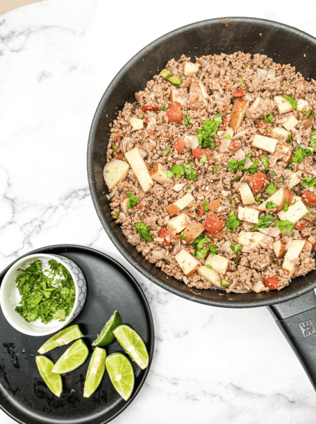 This Mexican Picadillo is made with ground beef, onion, jalapeños, chili powder, cumin, and garnished with cilantro and limes.