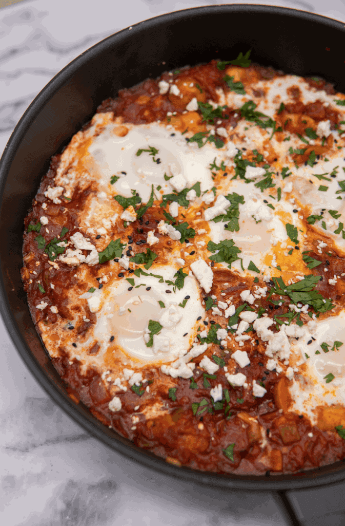 This Spicy Potato Shakshuka is made with spiced tomato sauce, harissa, poached eggs and garnished with cilantro and feta cheese!