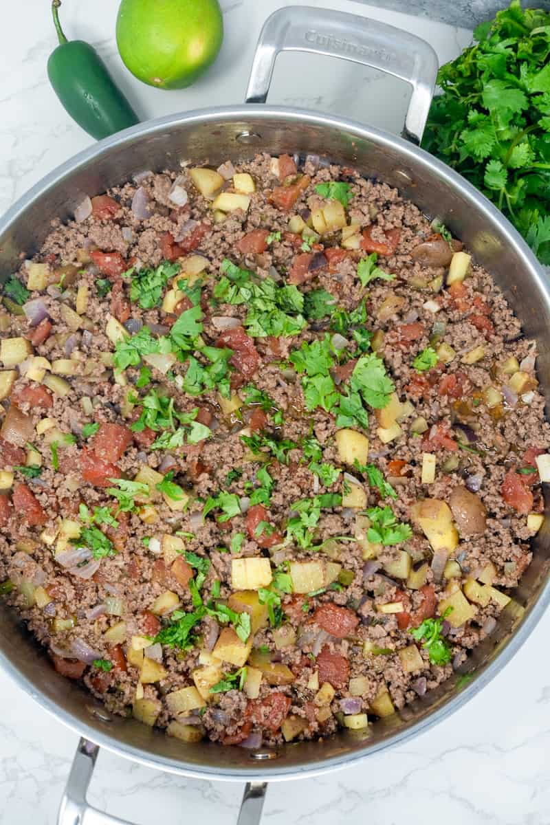 This Picadillo Recipe is made with ground beef, onion, jalapeños, chili powder, cumin, and garnished with cilantro and limes.