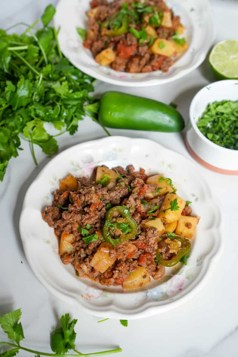 This Picadillo Recipe is made with ground beef, onion, jalapeños, chili powder, cumin, and garnished with cilantro and limes.