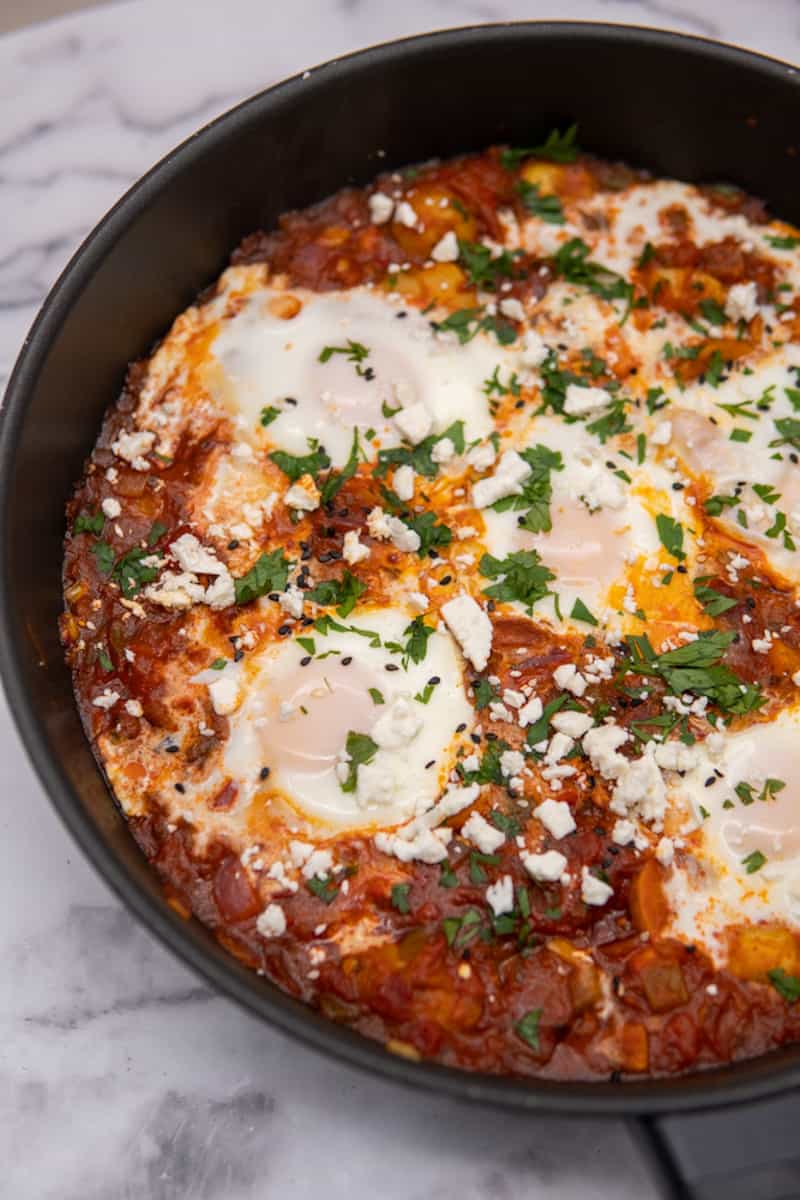 This Potato Shakshuka Recipe is made with spiced tomato sauce, harissa, poached eggs and garnished with cilantro and feta cheese!