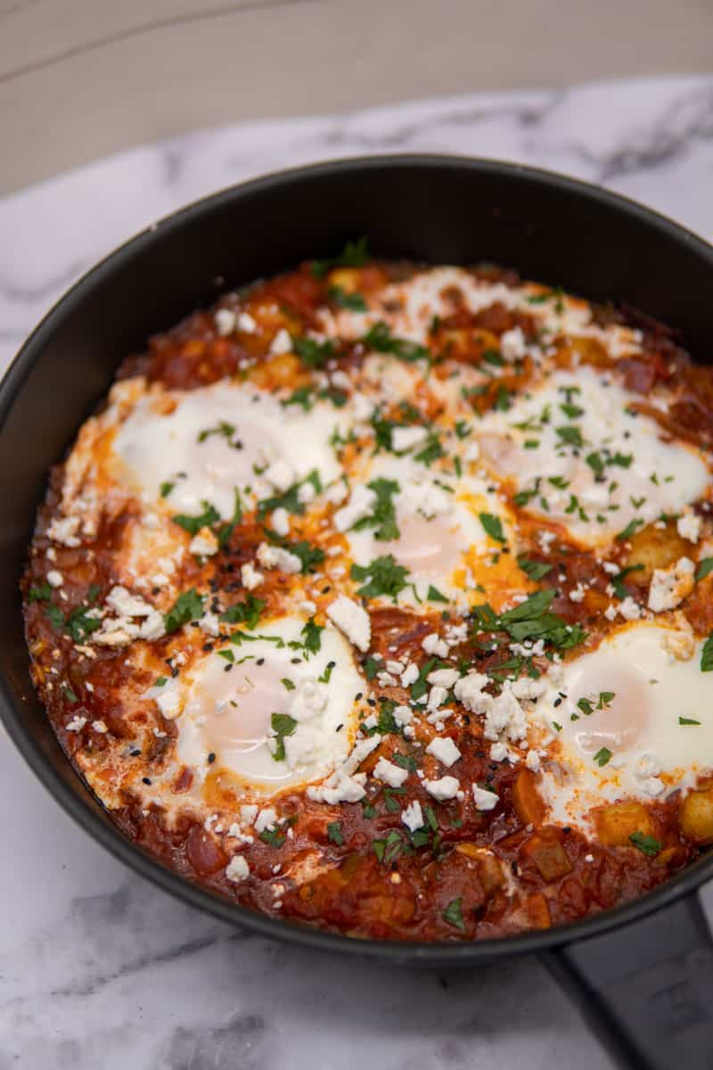 This Potato Shakshuka Recipe is made with spiced tomato sauce, harissa, poached eggs and garnished with cilantro and feta cheese!