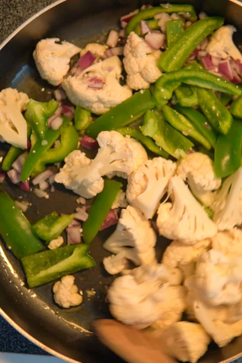 In a large deep saucepan, heat up the oil and add the onion, cauliflower and peppers. Cook until the cauliflower starts to brown and the onion and peppers are soft, about 10-15 minutes.