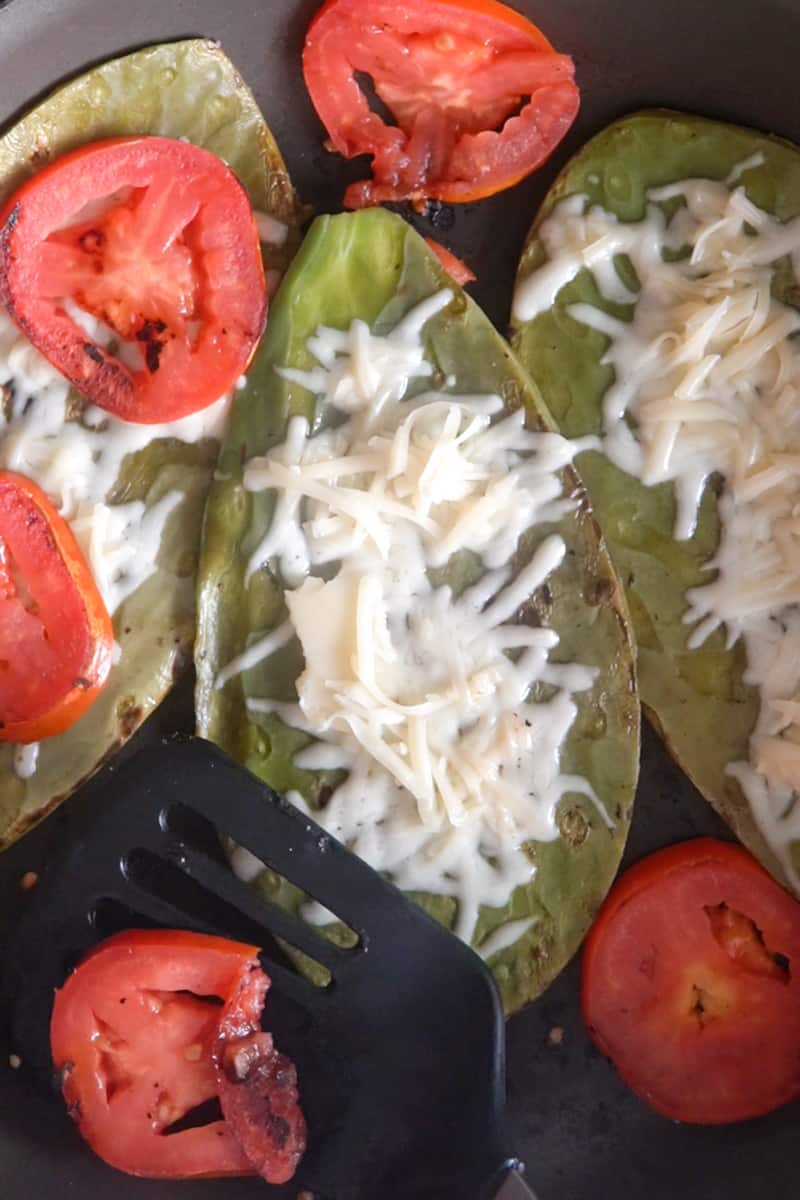 Lower to medium heat, then flip the nopales and add four slices tomato on the skillet (I like to use two slices for each nopal). 