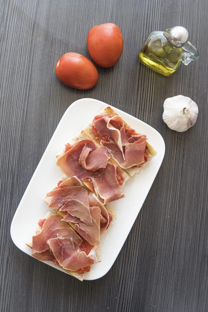 This Pan con Tomate Recipe is made with Roma tomatoes, olive oil, garlic, salt, crusty bread and topped with jamón serrano.