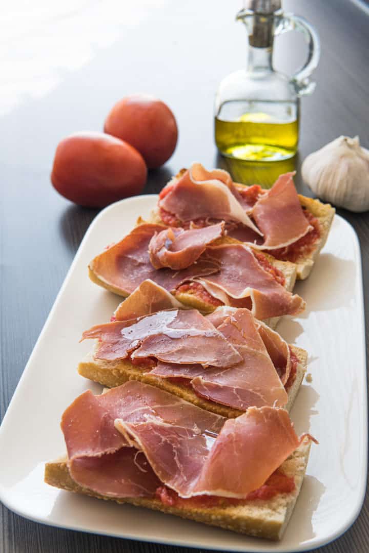 This Pan con Tomate Recipe is made with Roma tomatoes, olive oil, garlic, salt, crusty bread and topped with jamón serrano.