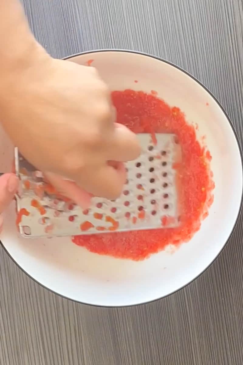 Start by washing the tomatoes and cutting them in half. Place the tomatoes on a cheese grater and grate them completely. Throw the skins away.