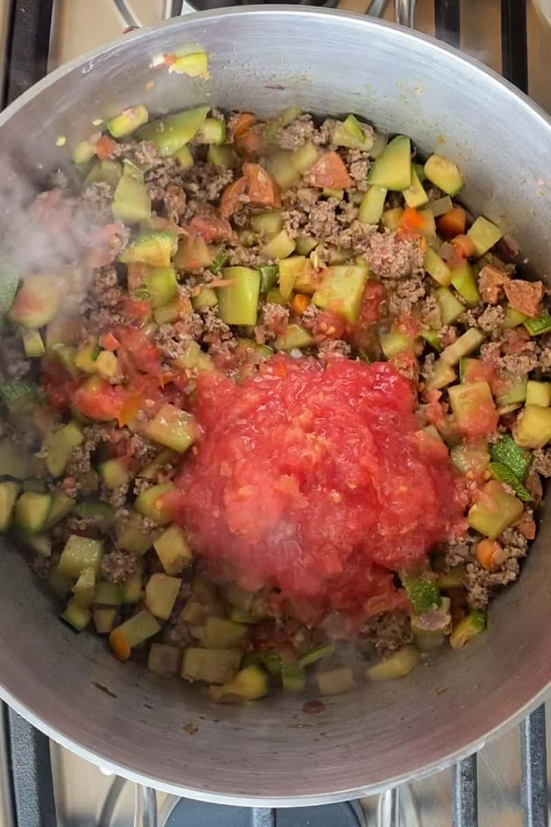Add the diced chorizo and ground beef to the pot and cook until the meat is browned and cooked through, about 5-7 minutes. Add the can of tomato sauce (or grated Roma tomatoes) to the pot and stir to combine.