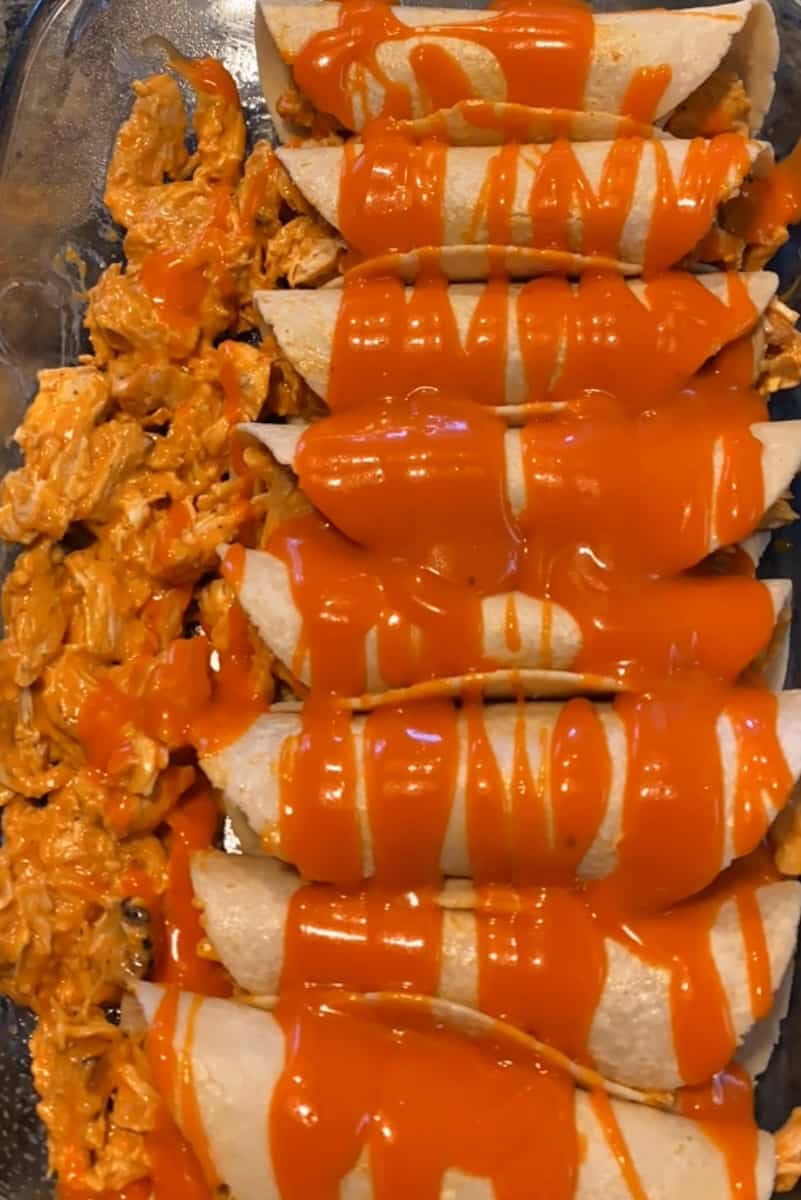 Assemble the remainder of the enchiladas, packing them into the baking dish. When they are all assembled, drizzle the remaining buffalo sauce and the ranch over all of them. Sprinkle cheese on top.