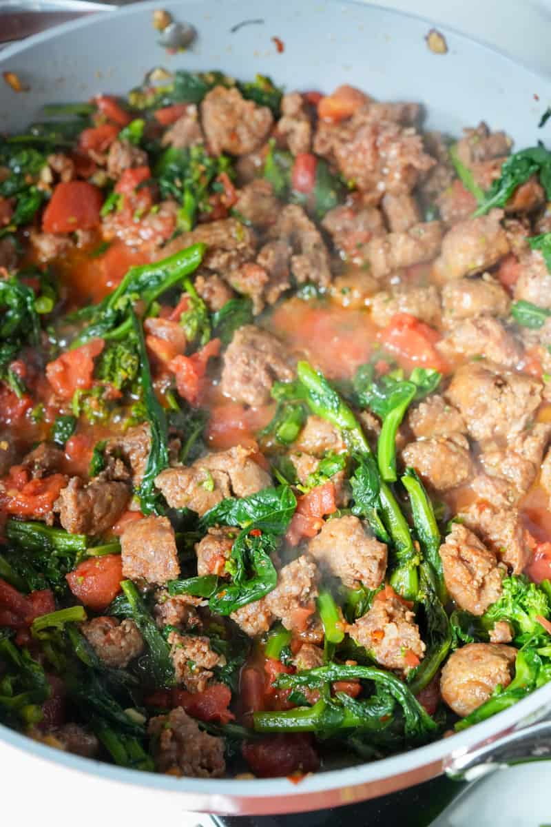 Pour in the diced tomatoes. Cook for 4 minutes and add the blanched broccoli rabe into the sausage mixture. Add salt, pepper and red pepper flakes to your liking. Keep simmering until the sausage is cooked through, about an extra 10 minutes. The sausage will be ready when the outside of the sausages are a deep golden brown and the inside is pale but with no sign of pink.