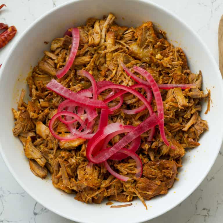 This Slow Cooker Cochinita Pibil dish is made with pork shoulder, achiote paste, oranges, limes, pickled onion, cilantro and served on gorditas. 