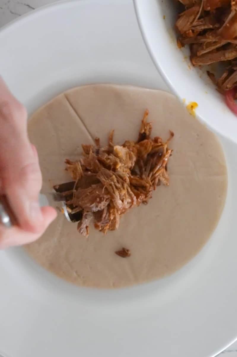 Place an empanada dough disc down and add two tablespoons of the meat mixture on it. Fold over and with a fork, press down to seal to prevent filling from getting out.