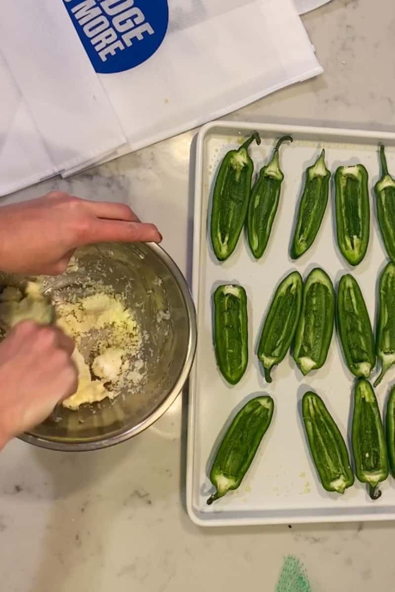 Add the cream cheese and finely grated cheddar cheese in a bowl and mix well with a fork. Take the halved and cored jalapeño and place the cheese mixture inside the pepper. Repeat with the rest.