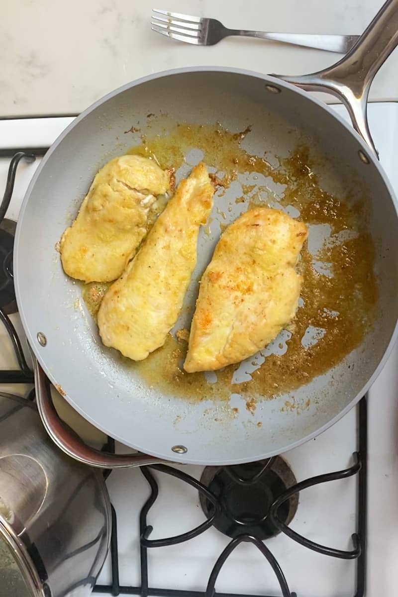 Rub chicken with olive oil, lemon zest, salt and pepper. In a shallow bowl, add flour. Dip the chicken in the oil mixture, then dredge the chicken on both sides. On a large pan on medium high, place olive oil and wait for it to shimmer. Add the chicken and sear the chicken until golden, about 5 minutes on each side. Remove the chicken. 