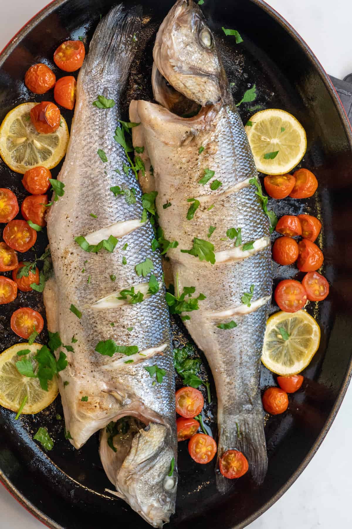 This Whole Roasted Branzino Recipe is made with whole branzino, olive oil, cherry tomatoes, lemon slices, butter, parsley and baked to perfection.