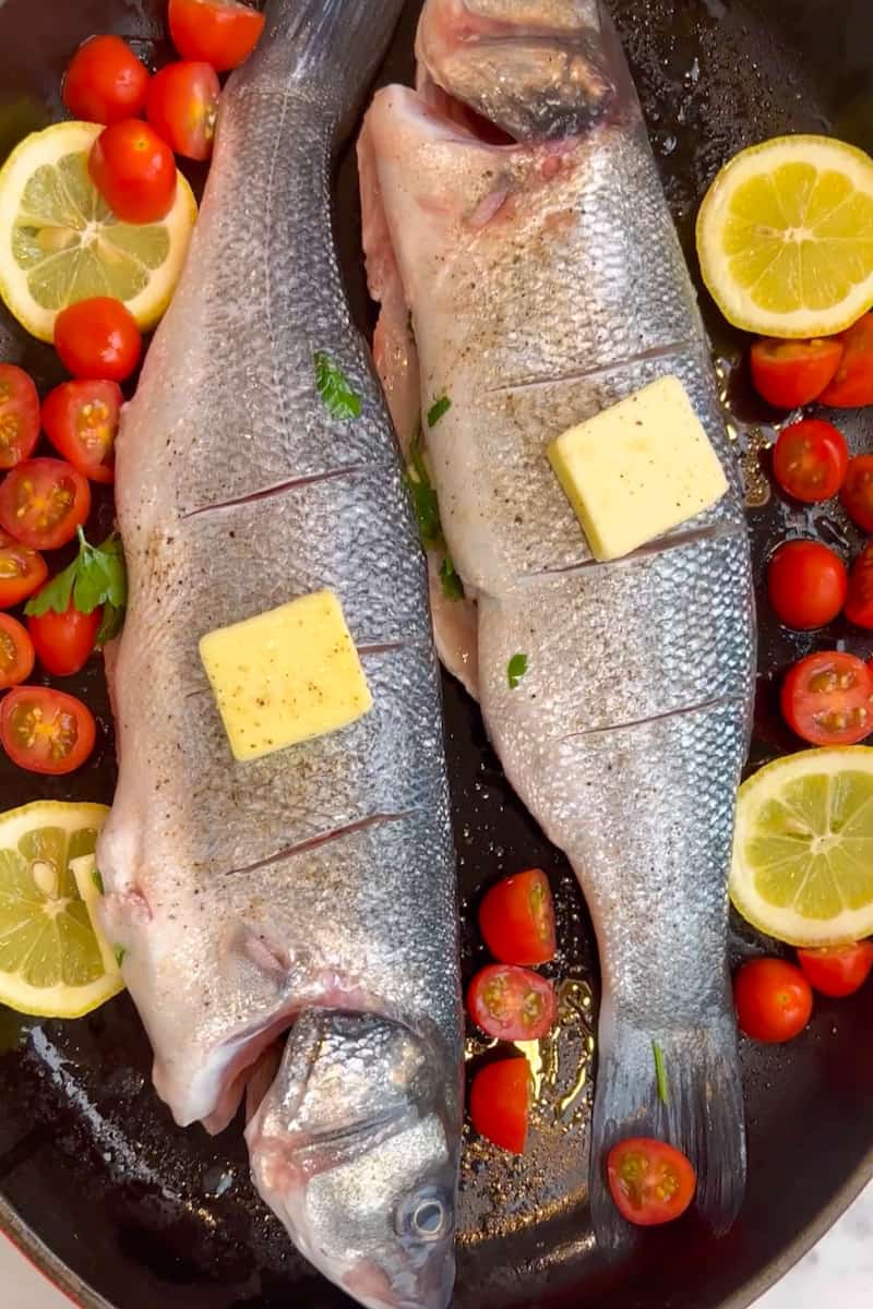 Transfer to a rimmed baking sheet. Scatter cherry tomatoes and lemon wedges around the fish. Place the last butter square on top of the fish.