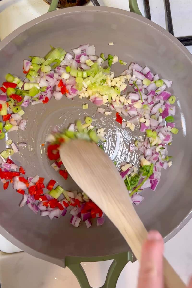 In a large skillet on medium-high heat, add oil and wait for it to shimmer. Add the diced red onion, garlic, Thai chili, lemongrass, and cilantro stems and cook until the garlic is onion is soft, about 5 minutes. 