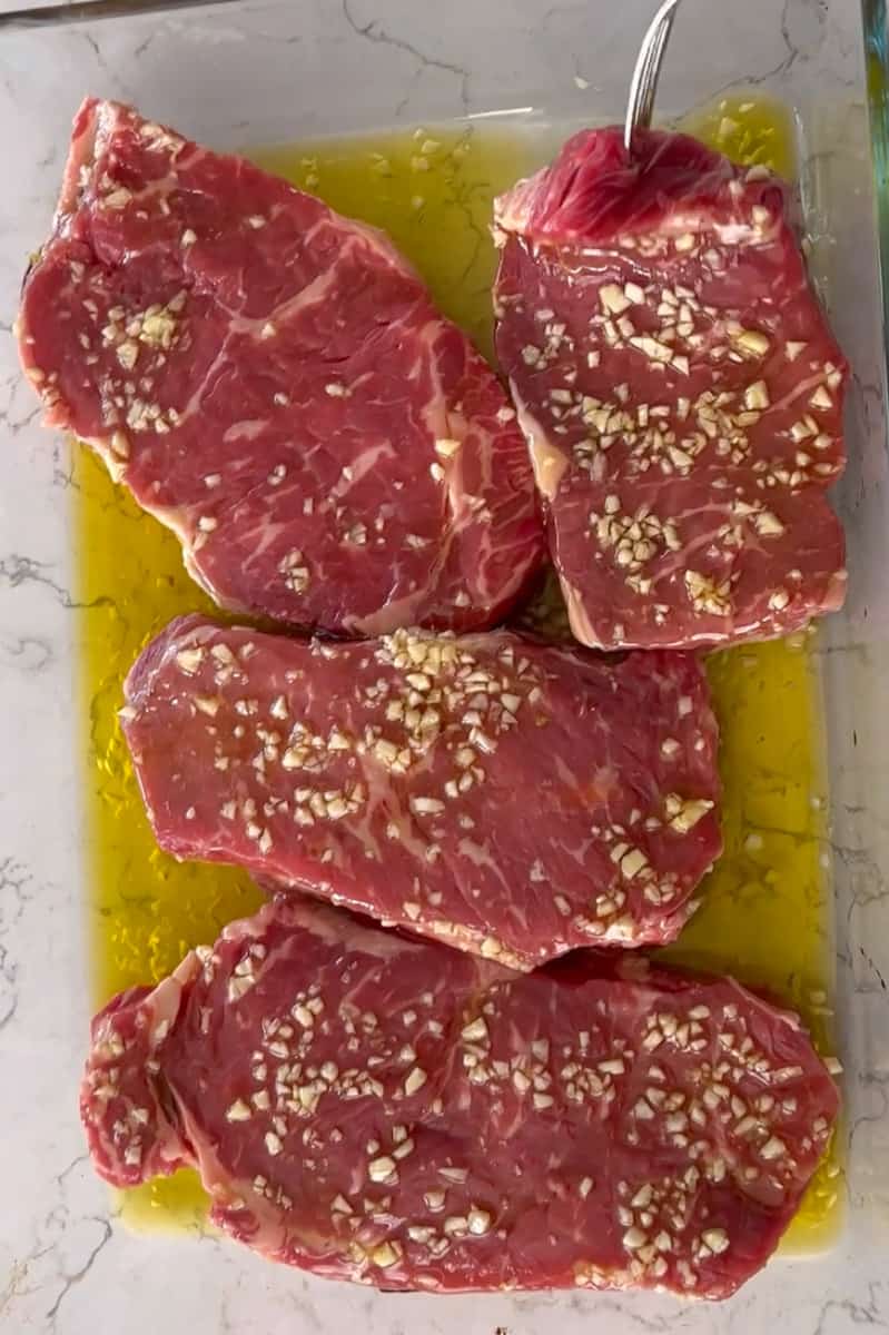 Taste the excess fat from the sides of the steak. Combine the oil and garlic in a baking dish and place the steaks in the baking dish, and let them stand for 15 minutes, flip and another 15 minutes.