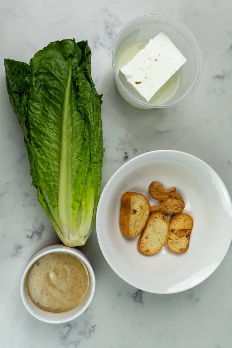 This Grilled Romaine Recipe with Feta is made with by grilling romaine lettuce and topping with Caesar dressing, croutons, and crumbled feta. 