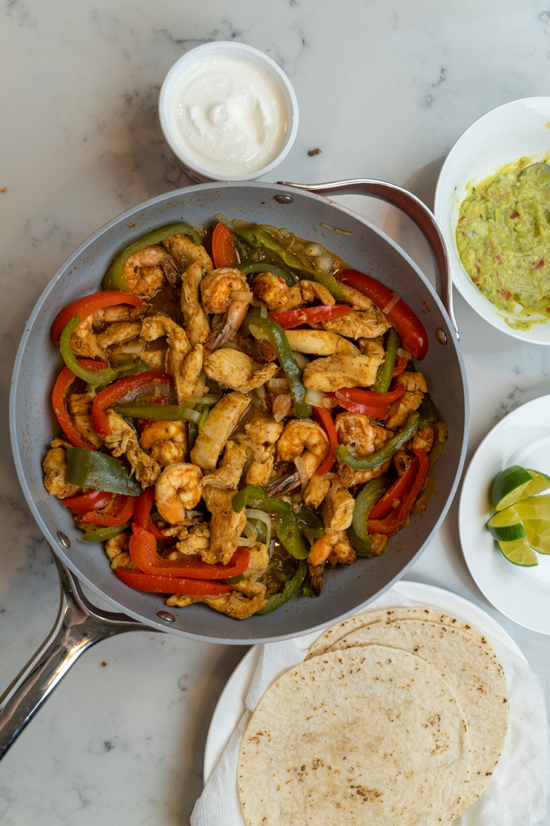 These chicken and shrimp fajitas are deliciously cooked with homemade taco seasoning and served with flour tortillas, sour cream, limes, and guacamole.