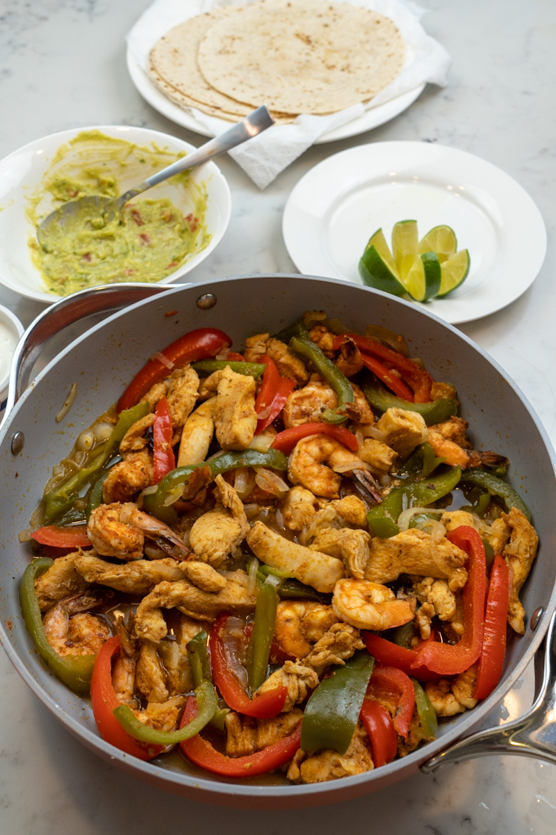 These chicken and shrimp fajitas are deliciously cooked with homemade taco seasoning and served with flour tortillas, sour cream, limes, and guacamole.