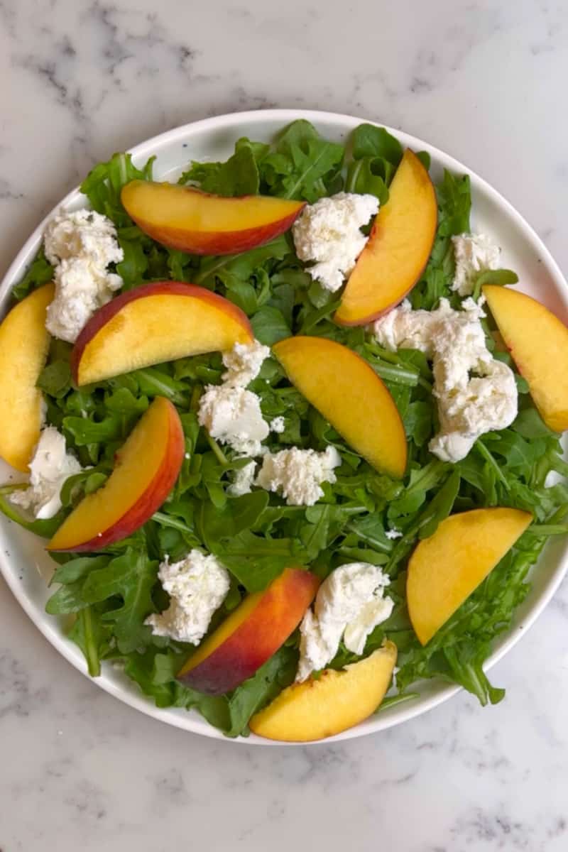 Scatter the peach wedges and burrata over the arugula.